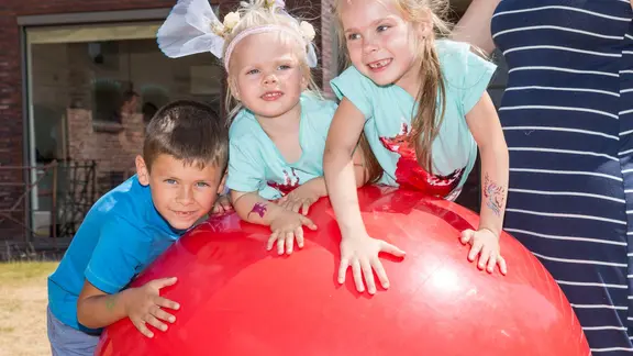 3 kinderen leunen en zitten op de reuzebal